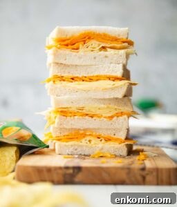 4 cheese sandwich halves stacked on each other on wooden board surrounded by crisps
