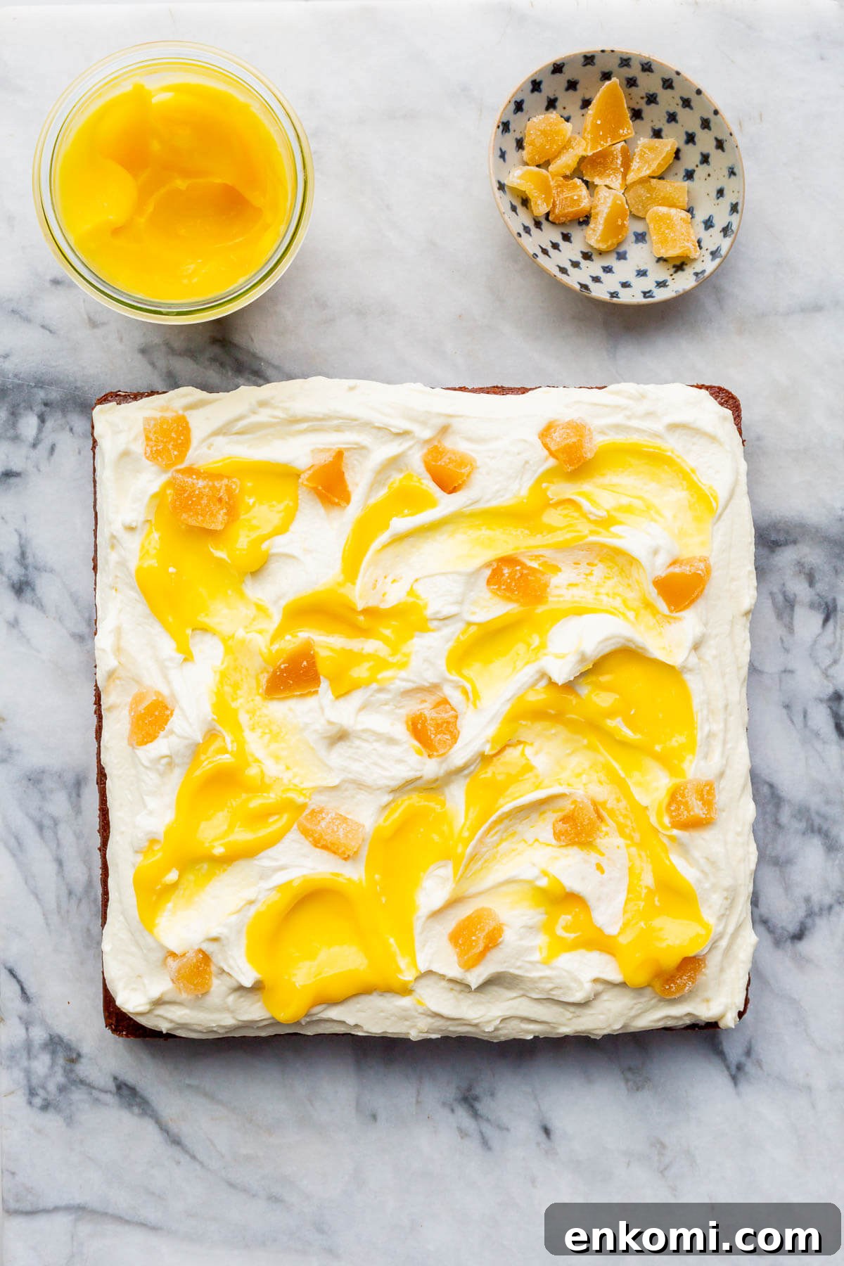 A square gingerbread cake topped with cream cheese frosting and lemon curd on a marble surface.