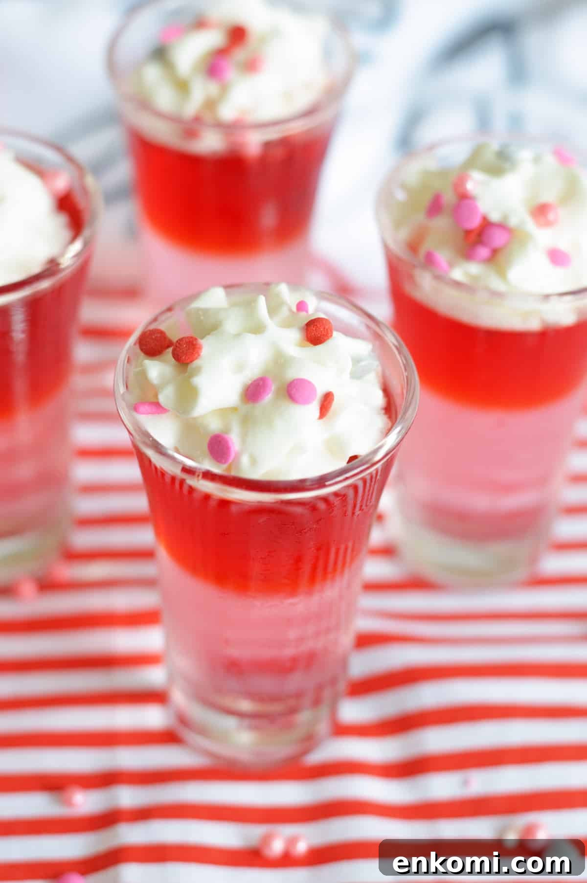 Red and pink layered Jello Shots toped with whipped cream and pink and red confetti sprinkles