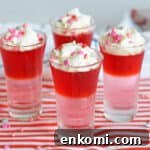 Four Valentine's Day Jello Shots with layers of red and pink gelatin and topped with whipped cream and Valentine's Day Sprinkles