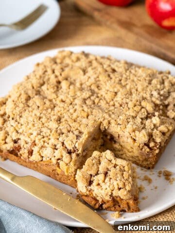 Applesauce crumb cake with a slice taken out on a white plate.