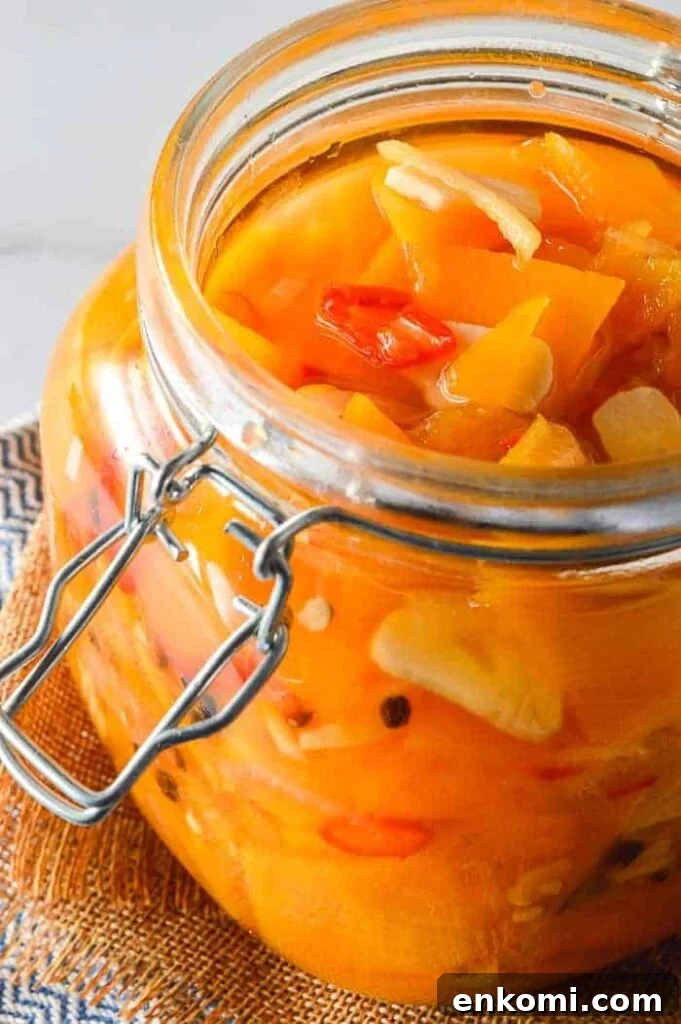 View into a glass jar with clear liquid, orange vegetable slices, garlic and red chilis