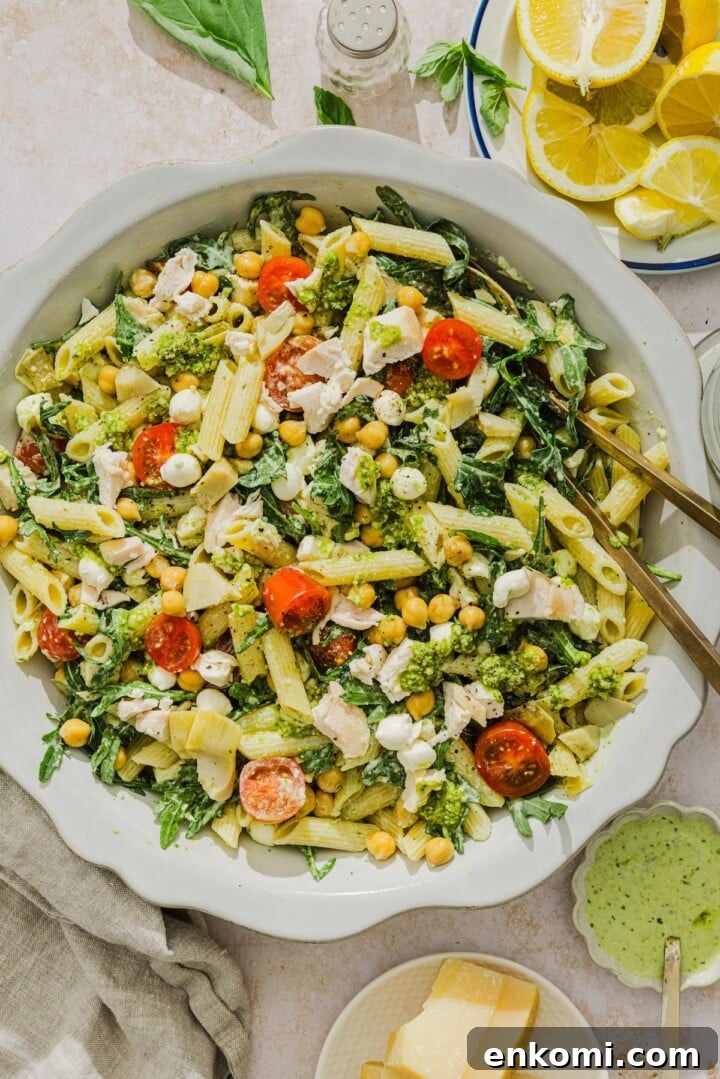 Chicken pesto pasta salad tossed on a scalloped white bowl.