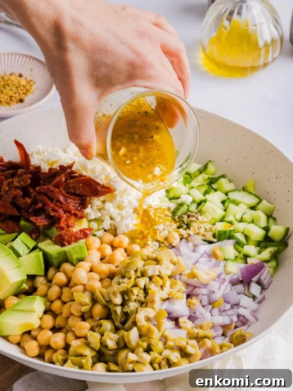 Chickpea Cucumber Feta Salad in a large, white serving bowl, with a woman's hand pouring dressing on top