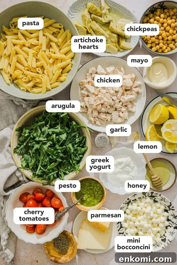 Ingredients for pesto chicken pasta salad displayed in small bowls on a marble counter.