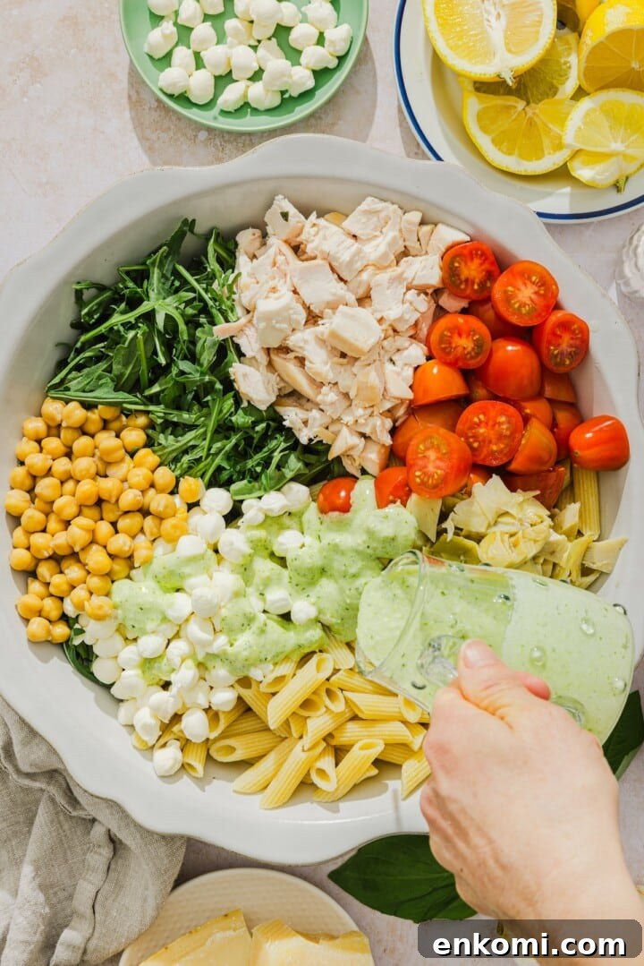 Creamy pesto dressing poured over pasta salad ingredients.