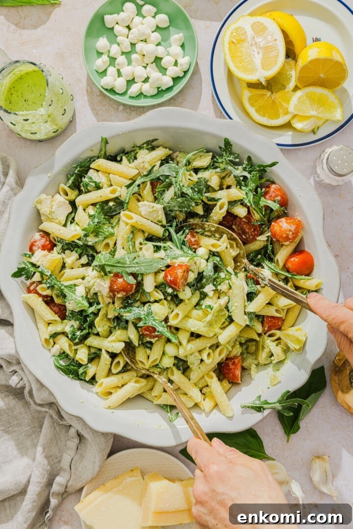 Creamy pesto pasta salad being tossed in a white bowl.