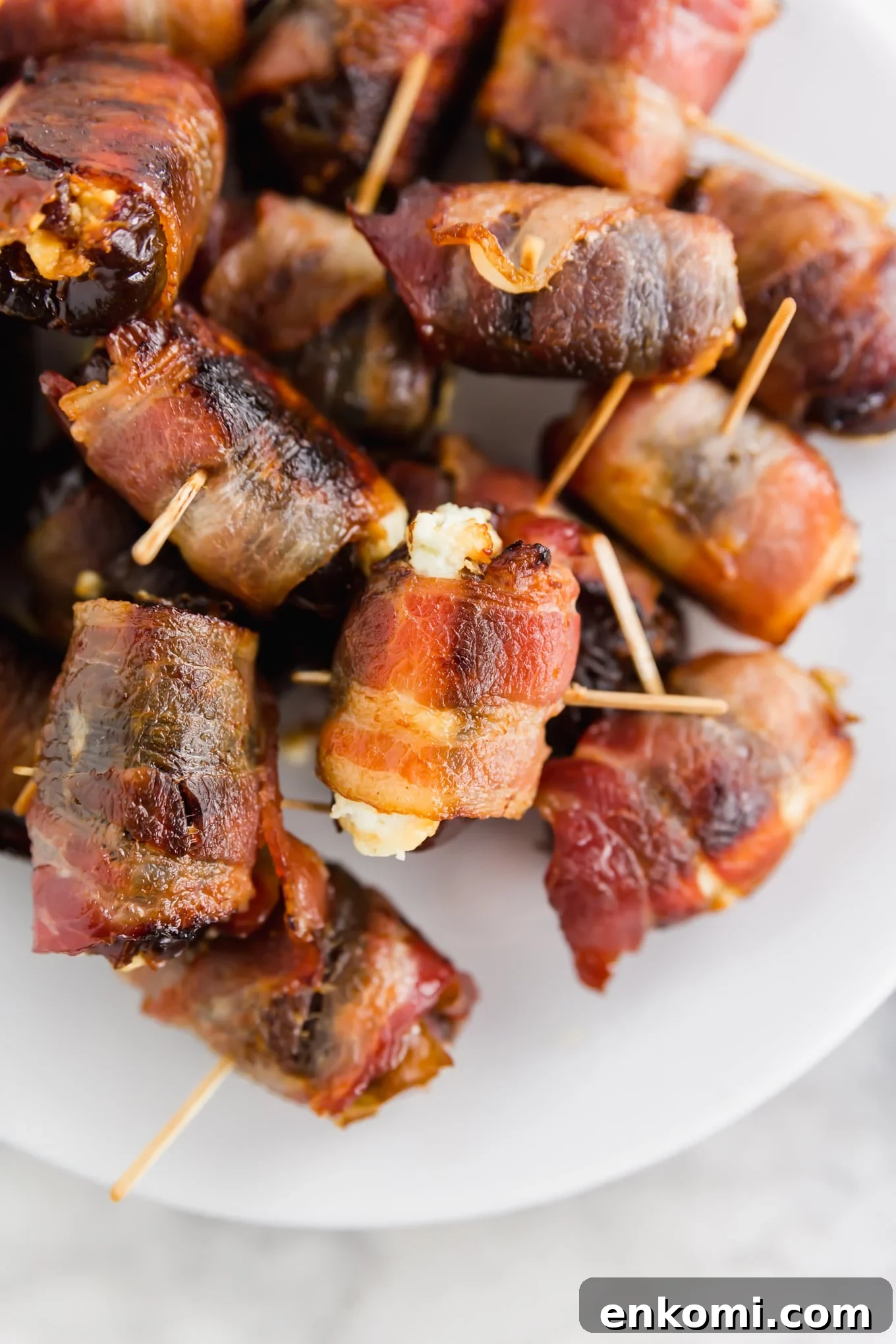 Bacon-Wrapped Dates Stuffed with Goat Cheese and Honey 2 A photo of 3-ingredient bacon wrapped dates with goat cheese with toothpicks inserted in the center on a platter.