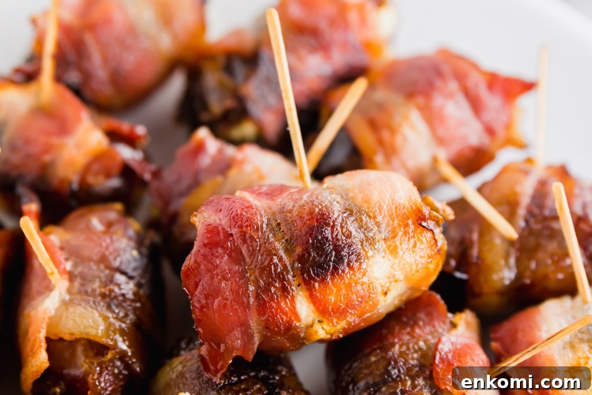 Bacon-Wrapped Dates Stuffed with Goat Cheese and Honey 3 Close-up of bacon wrapped dates with goat cheese and toothpicks on a serving platter showing crispy bacon.