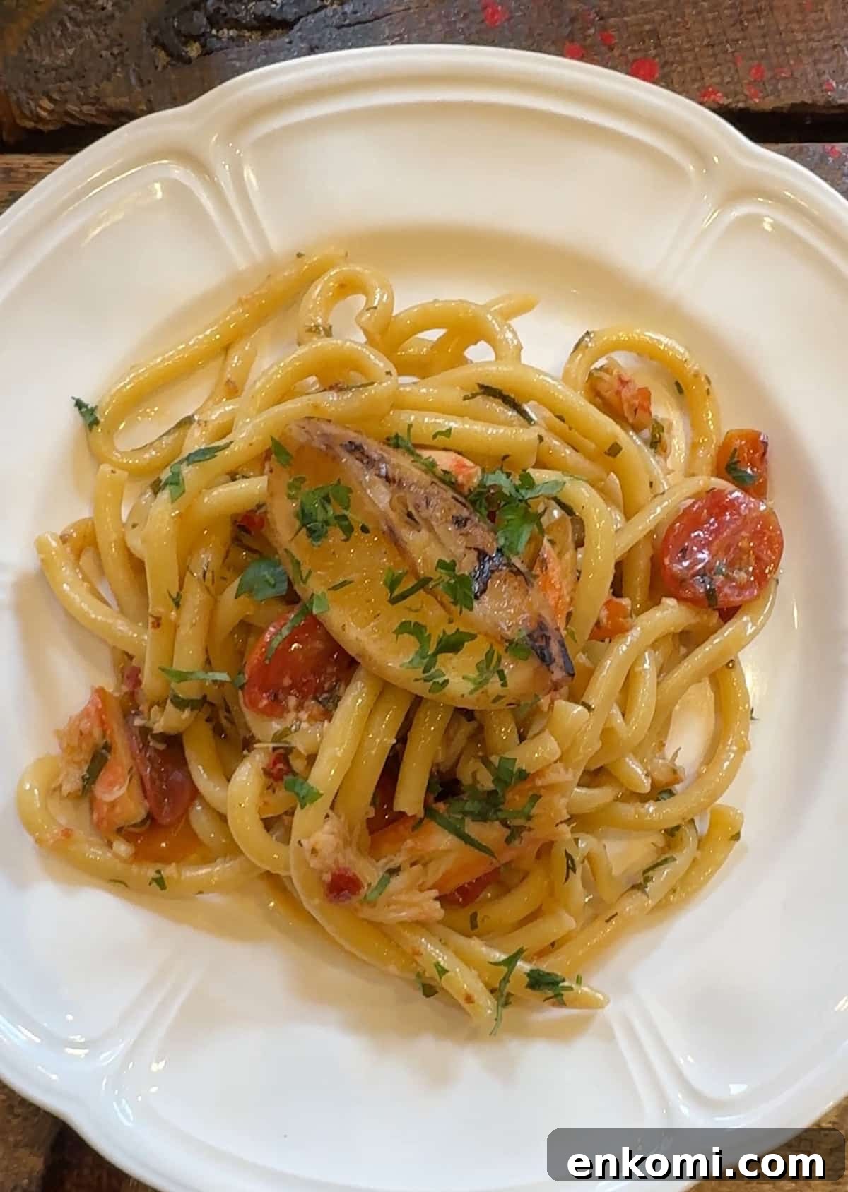 A plate of pasta with cherry tomatoes, herbs, and a slice of grilled seafood, served on a white dish.