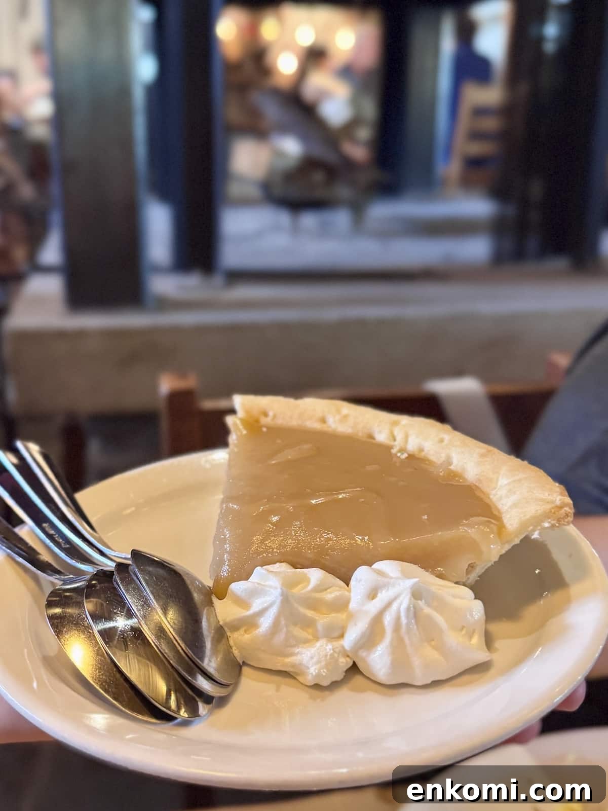 A slice of cream pie with two dollops of whipped cream served on a white plate with three metal spoons.