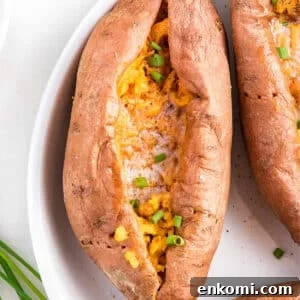 A cut open microwave sweet potato in a white dish and topped with melted butter and green onions.