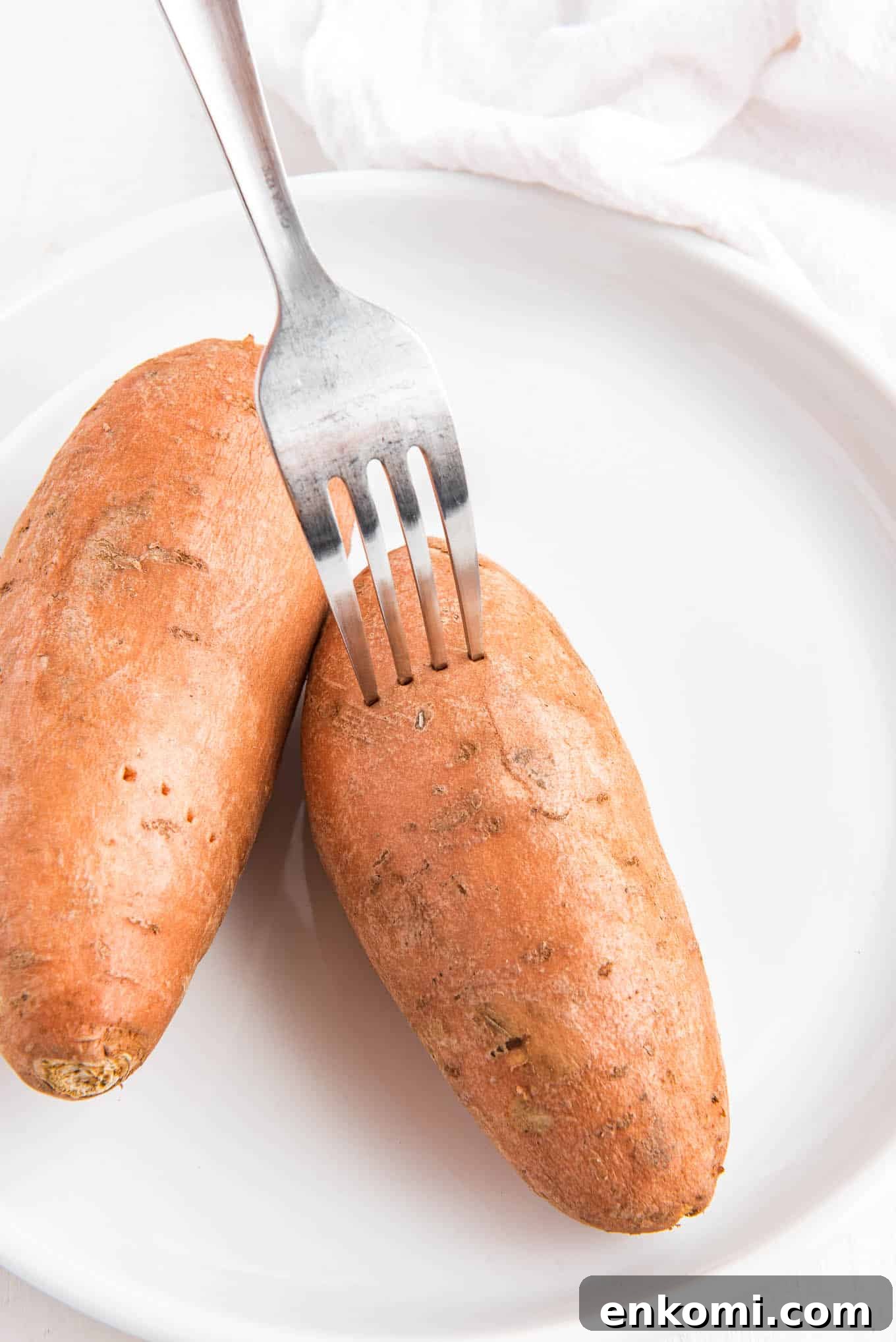 A fork piercing holes in the sweet potatoes on a plate.