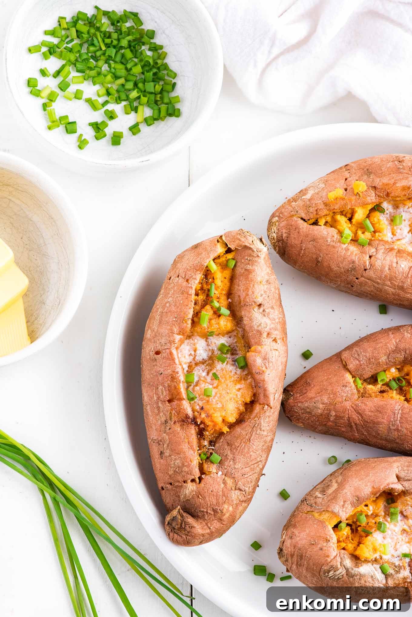 Sweet potatoes cooked and cut open topped with spices and butter in a casserole dish with a bowl of butter in a dish.