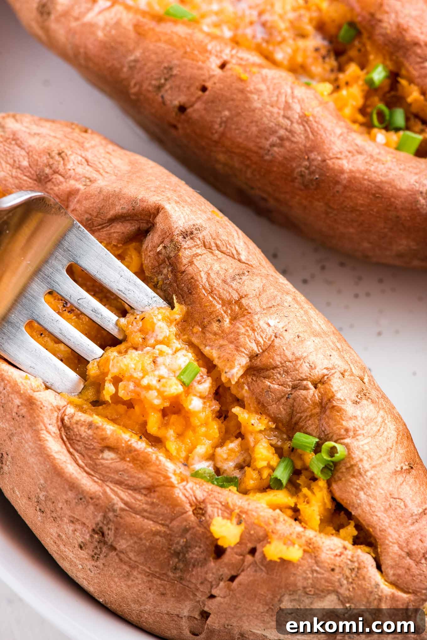 A microwave sweet potato on a plate with a fork scooping up a bit from the center.