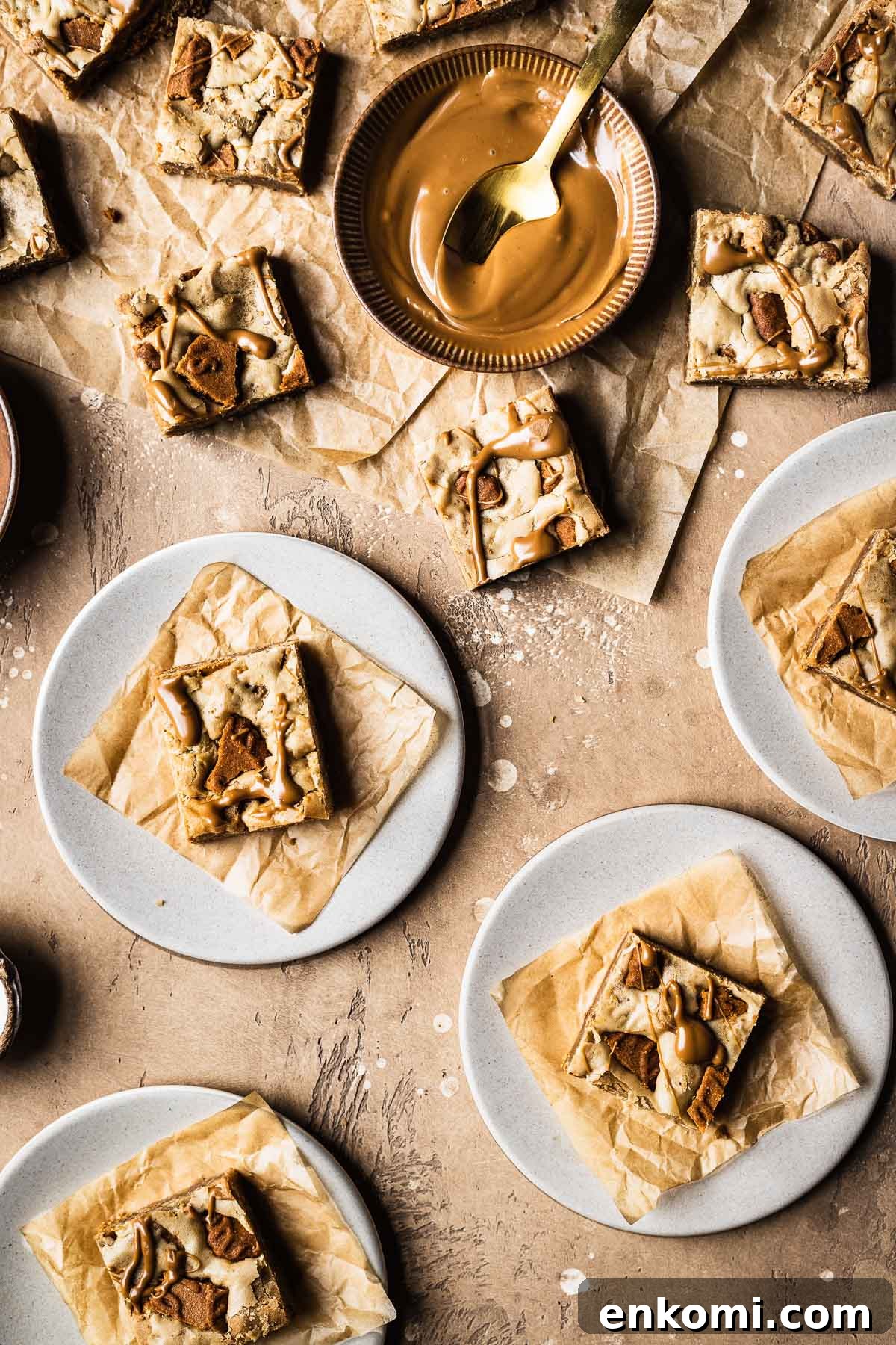 Biscoff Blondie Bars with Cookie Butter Swirl 11 Plates of sliced bar cookies on brown parchment squares with a small bowl of biscoff spread nearby.