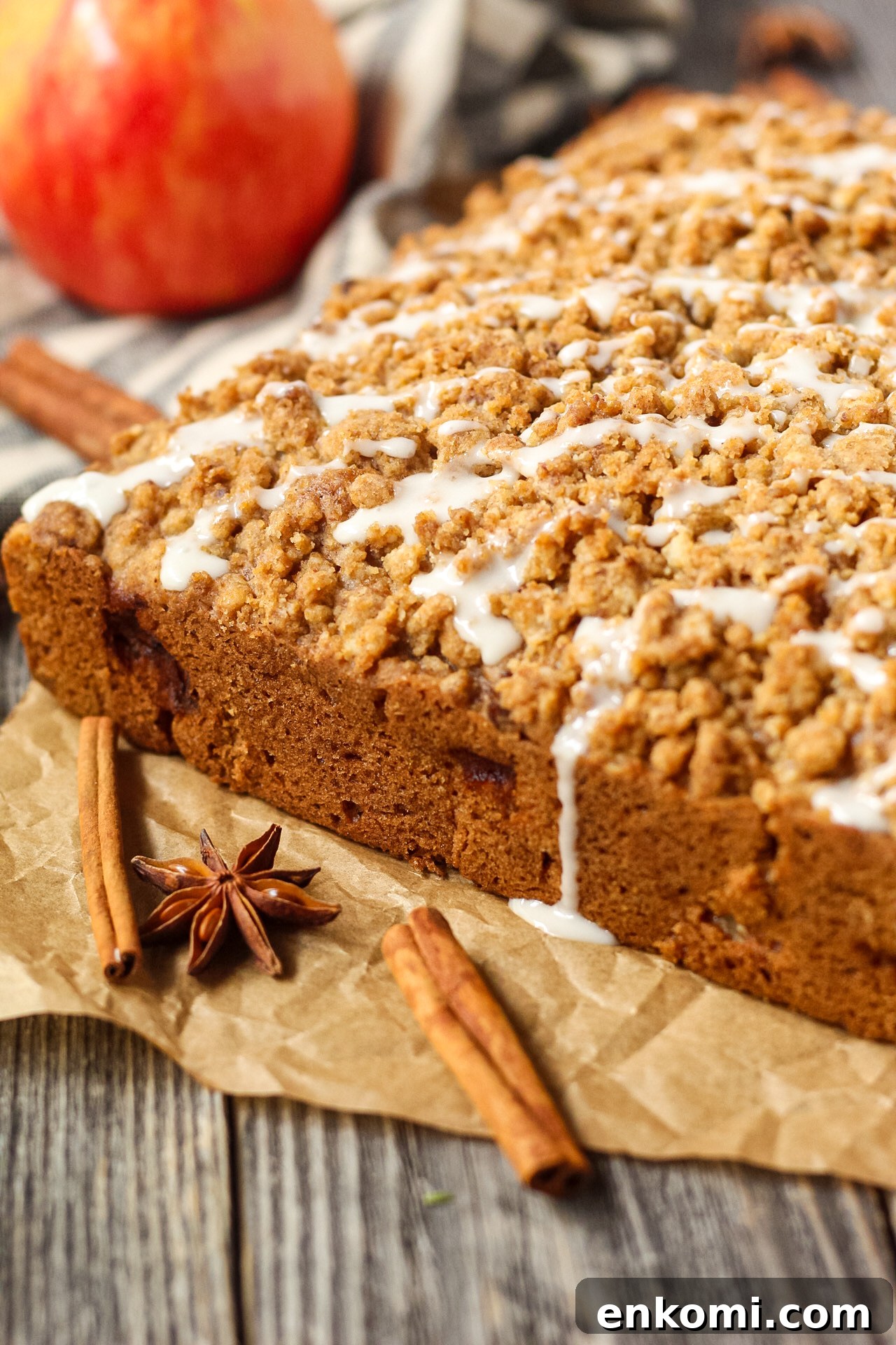 side shot of spiced apple crumb cake on wooden suface wiht an apple in the background.  