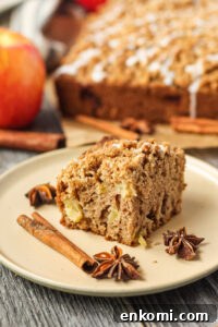 side shot of slice of apple crumb cake on a brown plate with apples and more cake in the background.