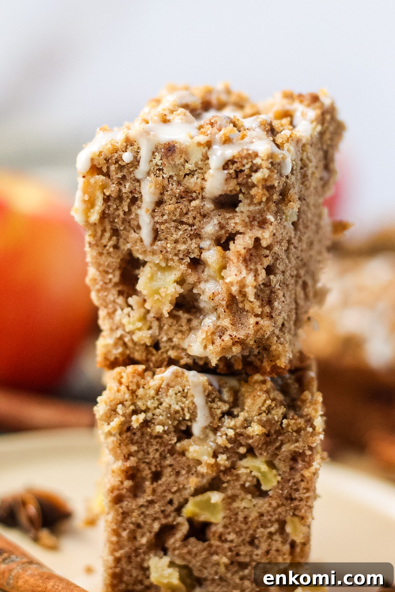 close up side shot of two slices of spiced apple crumb cake stacked on a brown plate with apples, cinnamon stick and star anise pods in the perimeter of shot.