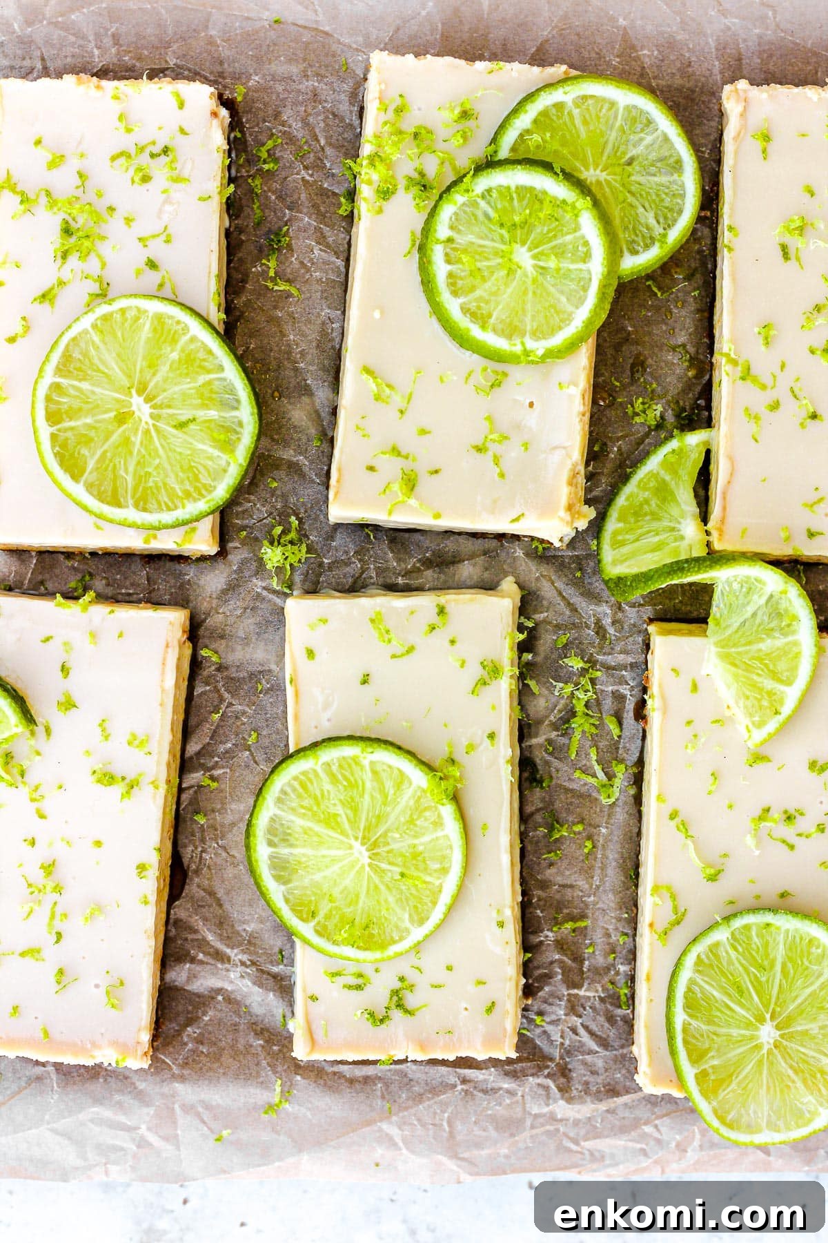 Key lime pie bars with fresh lime slices and lime zest on brown parchment paper.