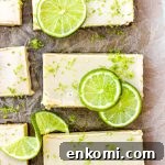 Key lime pie bars with fresh lime slices and lime zest on brown parchment paper.