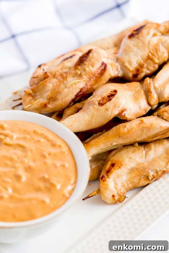 Chicken skewers on a plate next to a bowl of Thai dipping sauce.