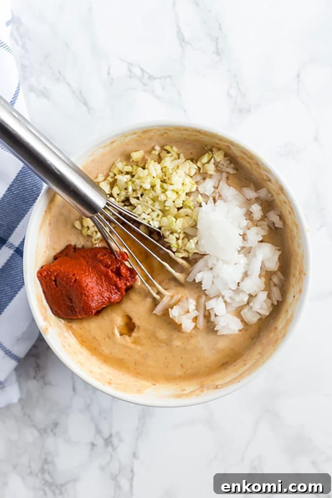 ingredients to make creamy peanut sauce in a white bowl with a small whisk