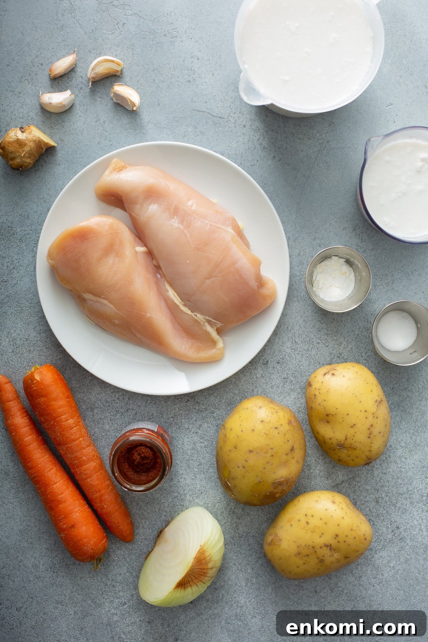 Ingredients for chicken curry. There are three peeled potatoes, two carrots, two chicken breasts, and curry paste, garlic, onion, cream, and salt.