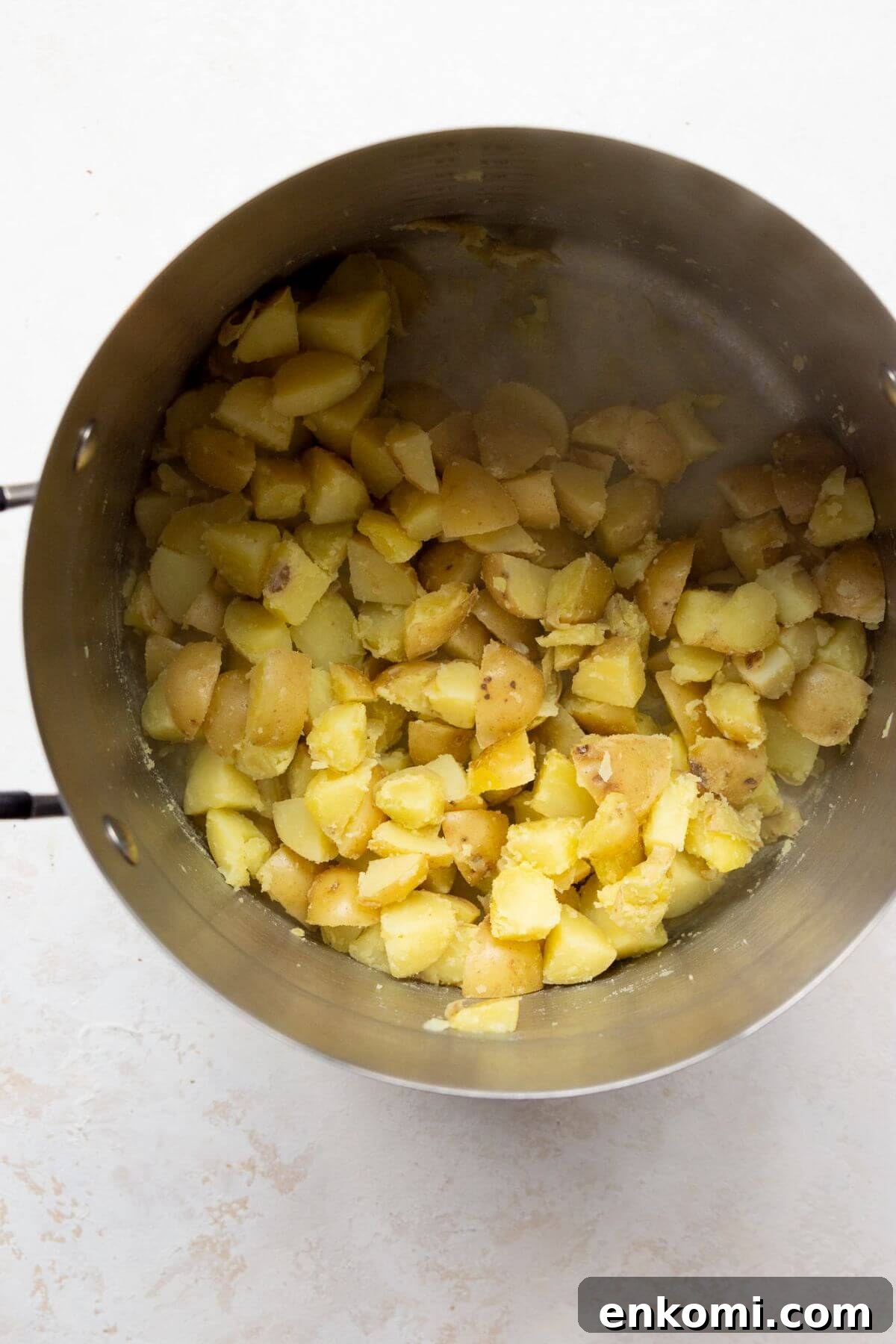 Parboiled potatoes in a pot with fluffy, roughed-up edges after shaking, ready for roasting.