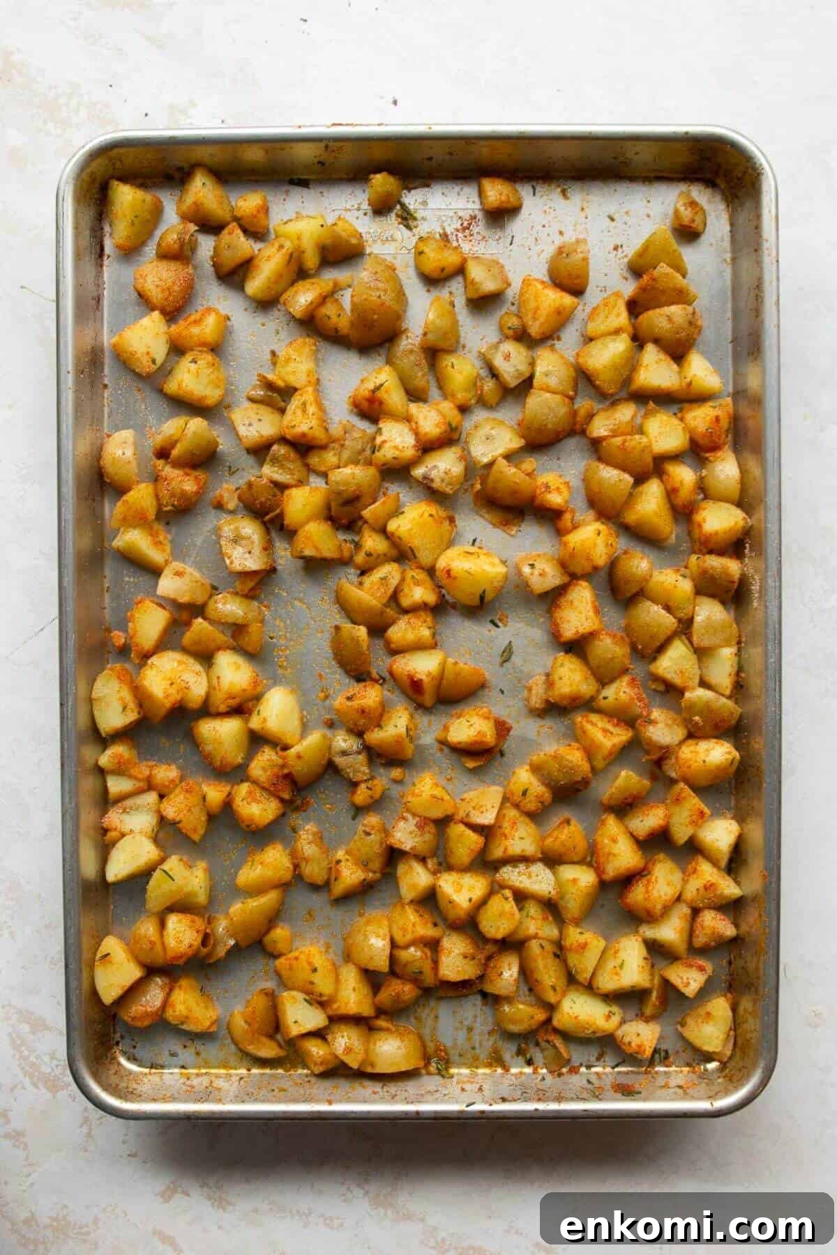 Seasoned potato cubes spread in a single layer on a bare metal baking sheet before roasting at 425°F.