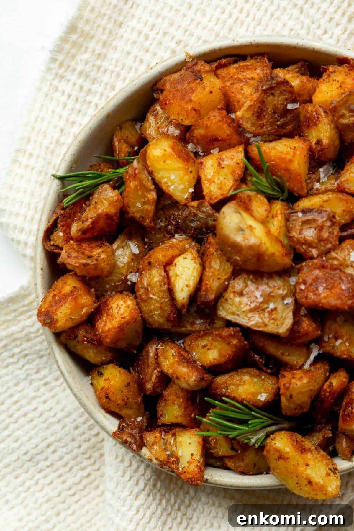 Crispy roasted potatoes piled in a serving bowl, topped with fresh rosemary and flaky salt.