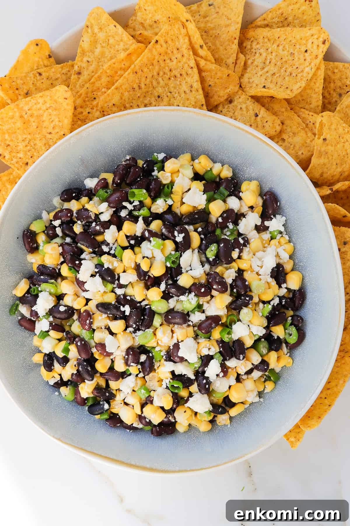 Corn, black bean feta dip in a bowl with tortilla chips on the side.