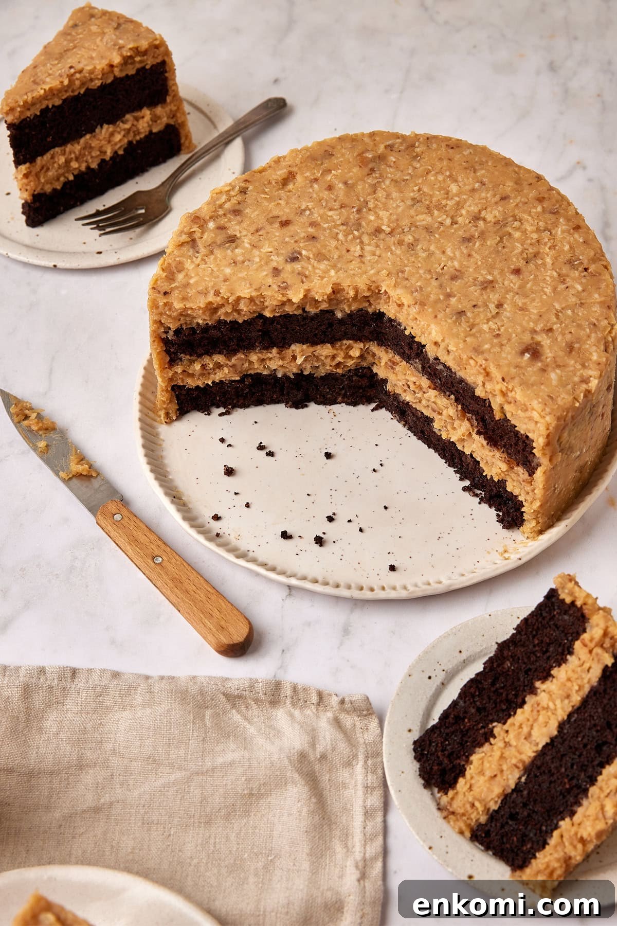 Keto German Chocolate Cake Recipe: Low-Carb Decadent Dessert 4 A 2/3 cut German Chocolate Cake with slices on plates, a napkin and a knife surrounding it on the countertop.