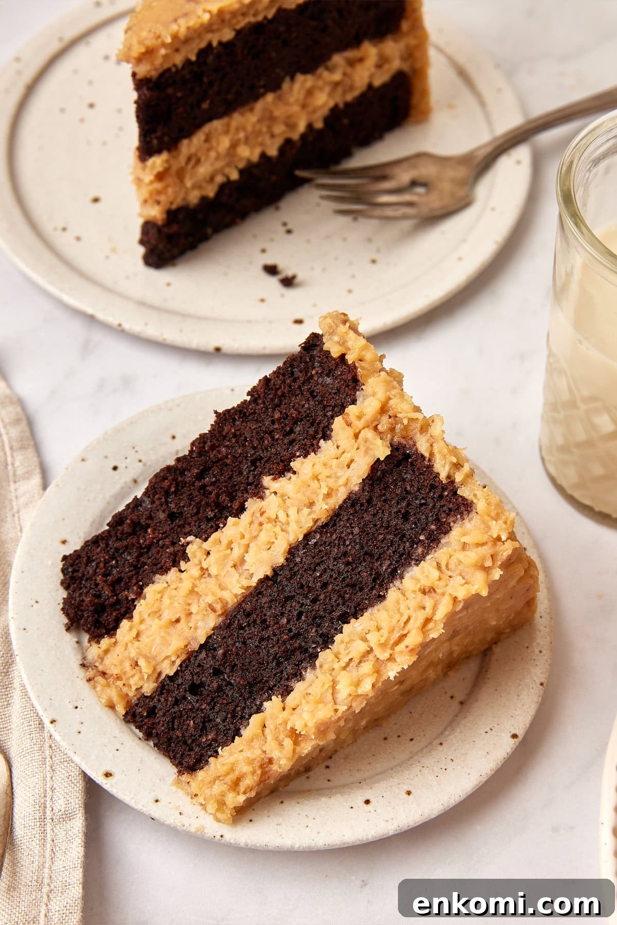 Keto German Chocolate Cake Recipe: Low-Carb Decadent Dessert 6 Thick slice of German Chocolate Cake on a white plate, with another slice on a plate with a fork in the background.
