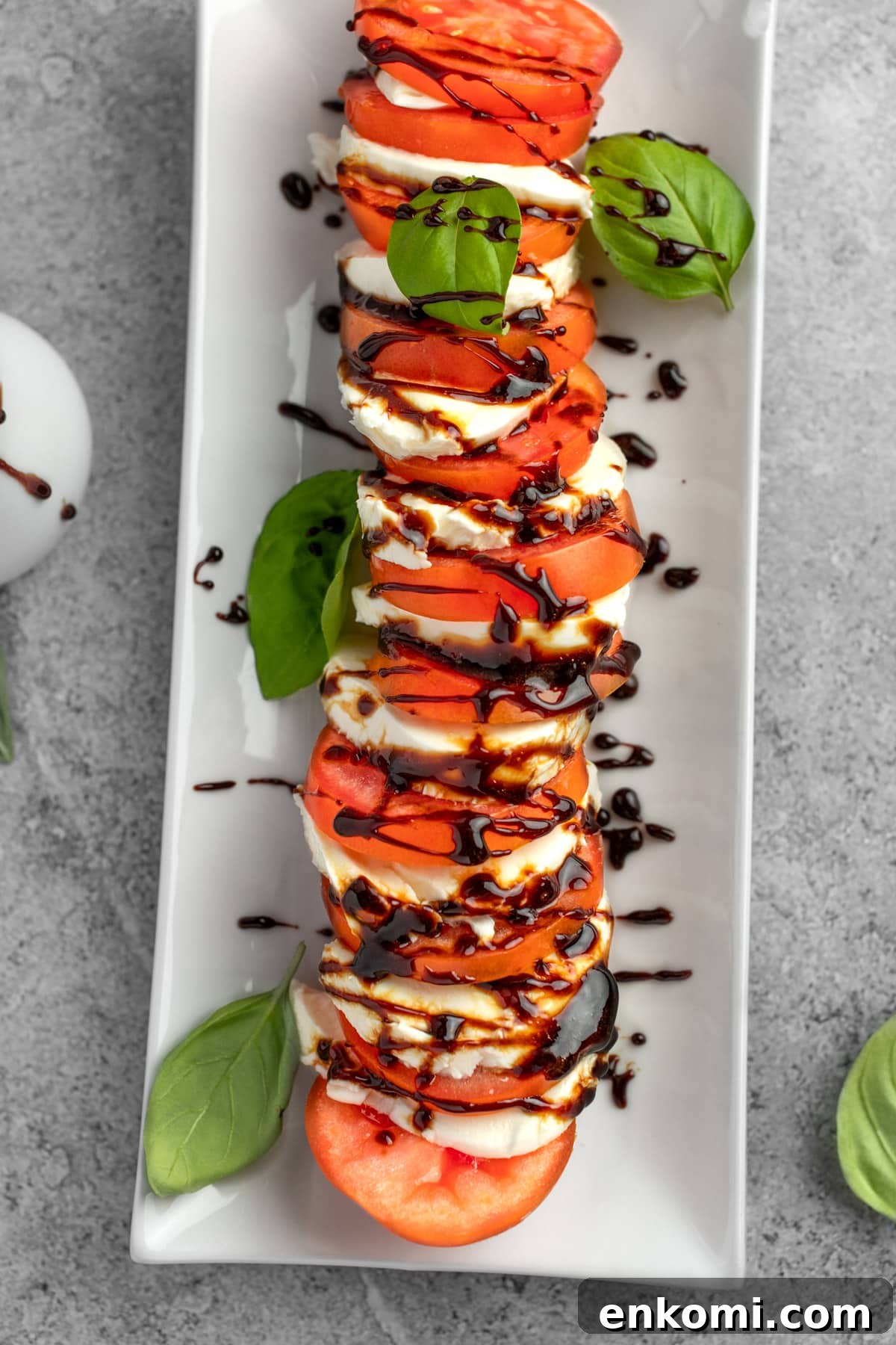 Balsamic Glaze Recipe for Caprese Salad Dressing 5 Caprese salad on a white rectangular plate, garnished with fresh basil leaves and drizzled with balsamic glaze.