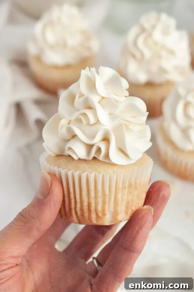 Dairy-Free Cream Cheese Frosting Recipe for Vegan Cakes 8 A hand is holding a vanilla cupcake that is topped with white fluffy buttercream frosting.