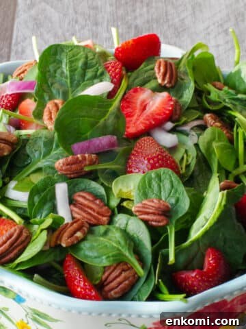 strawberry spinach pecan salad in a large bowl with flower print and wooden utensils