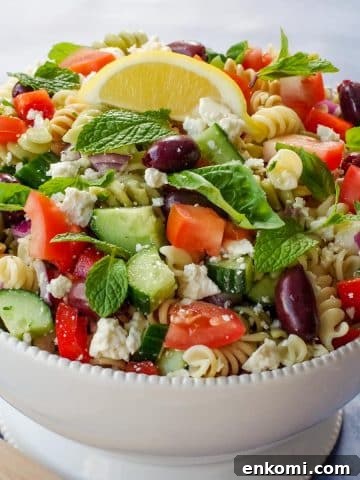 Greek Pasta salad in a white bowl with lemon wedge on top.