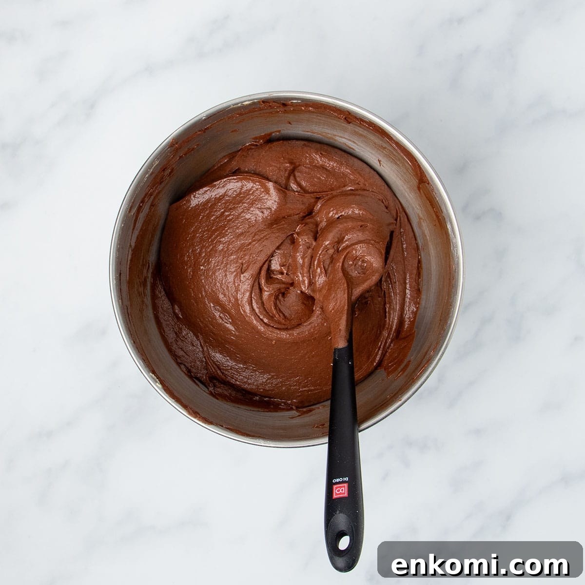 fully mixed raw brown soft cake batter with black spatula in bowl