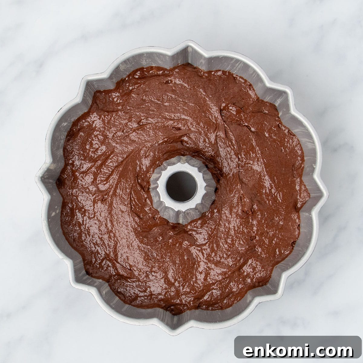 raw brown soft cake batter in classic silver cast aluminum bundt pan on marble surface