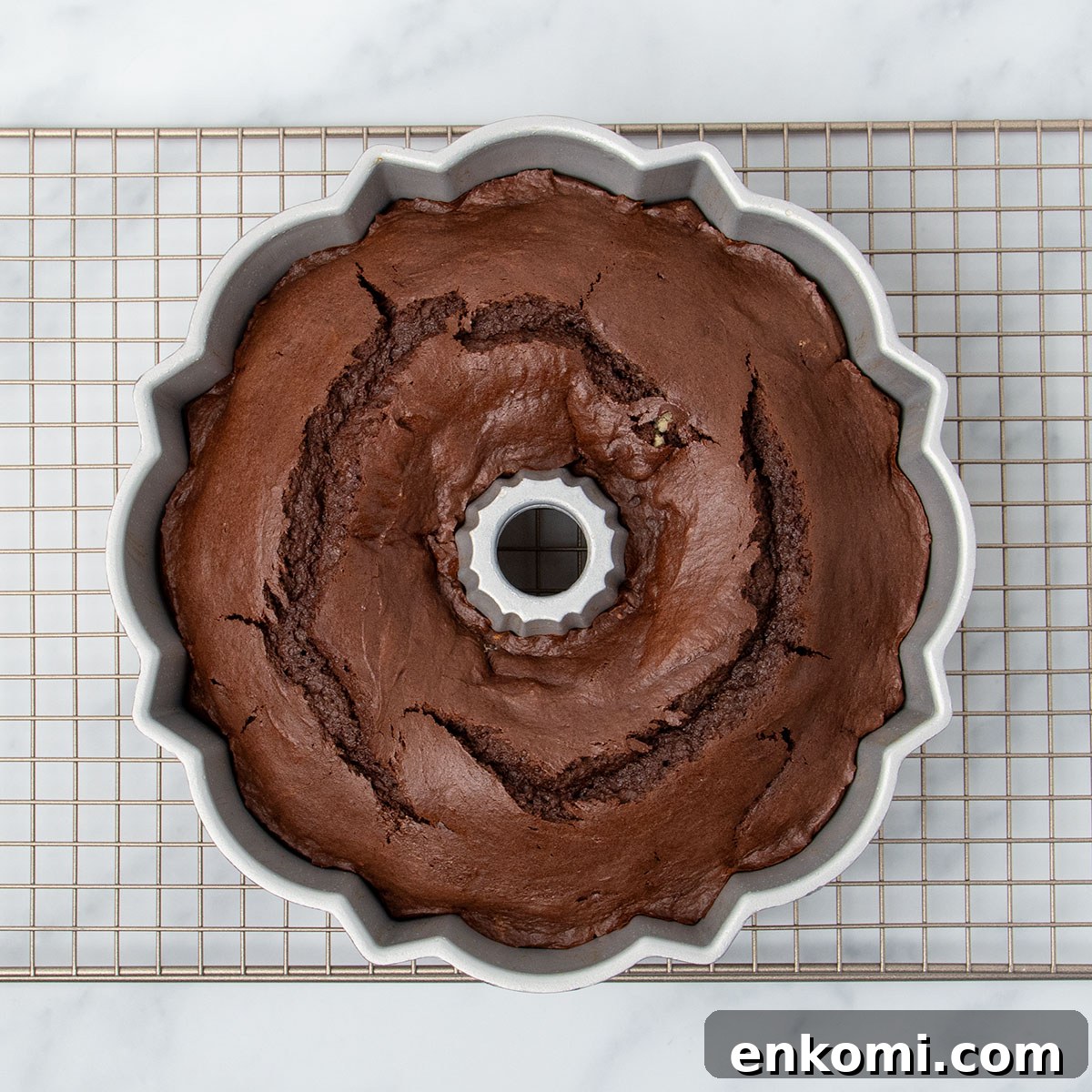 same pan with baked brown cake with fissures on top on gold wire rack