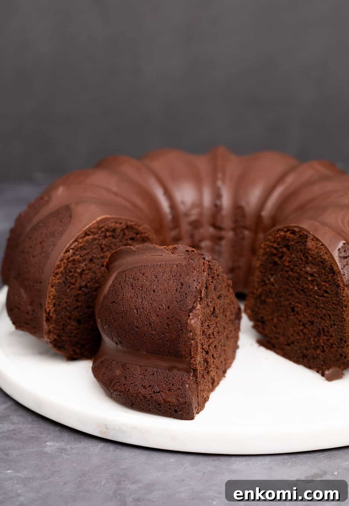 mostly whole round gluten free chocolate bundt cake with 2 slices cut, one missing and one on its side on round marble cake plate