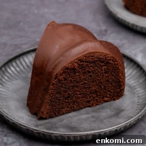 brown slice of gluten free chocolate bundt cake with hard chocolate icing on small gray fluted plate on gray surface