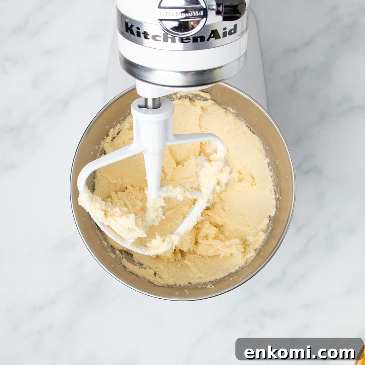 white kitchenaid stand mixer with tilt head tilted up with white paddle attachment with plate yellow whipped butter and sugar