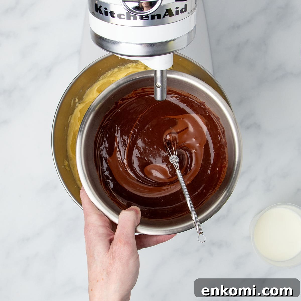 hand holding small round metal mixing bowl with soft dark chocolate mixture with very small wire whisk