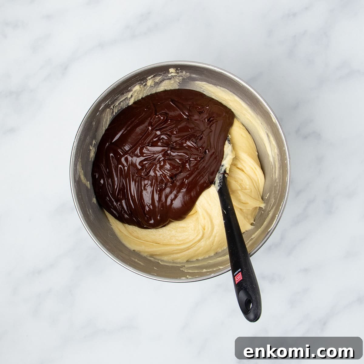 stand mixer bowl with yellow raw batter mixture with chocolate mixture on top, and black silicone spatula