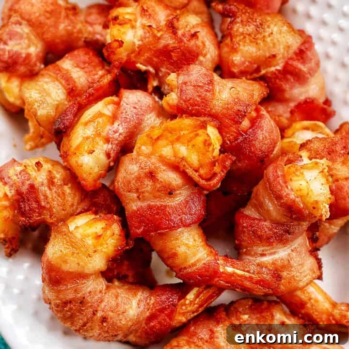 Crispy Air Fryer Bacon-Wrapped Shrimp Recipe 13 several bacon-wrapped shrimp stacked onto a white plate.