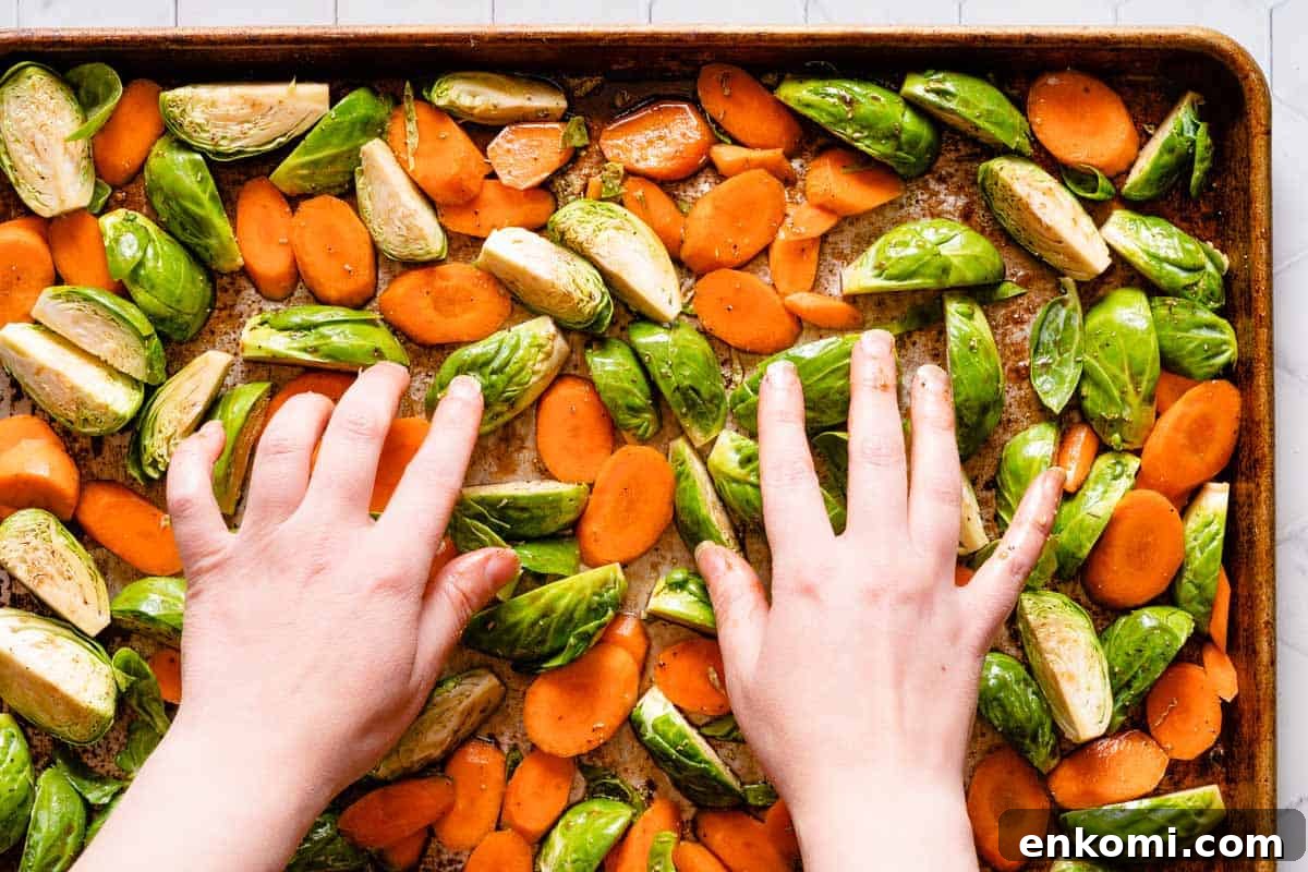 hands spreading out carrots and brussels sprouts on pan