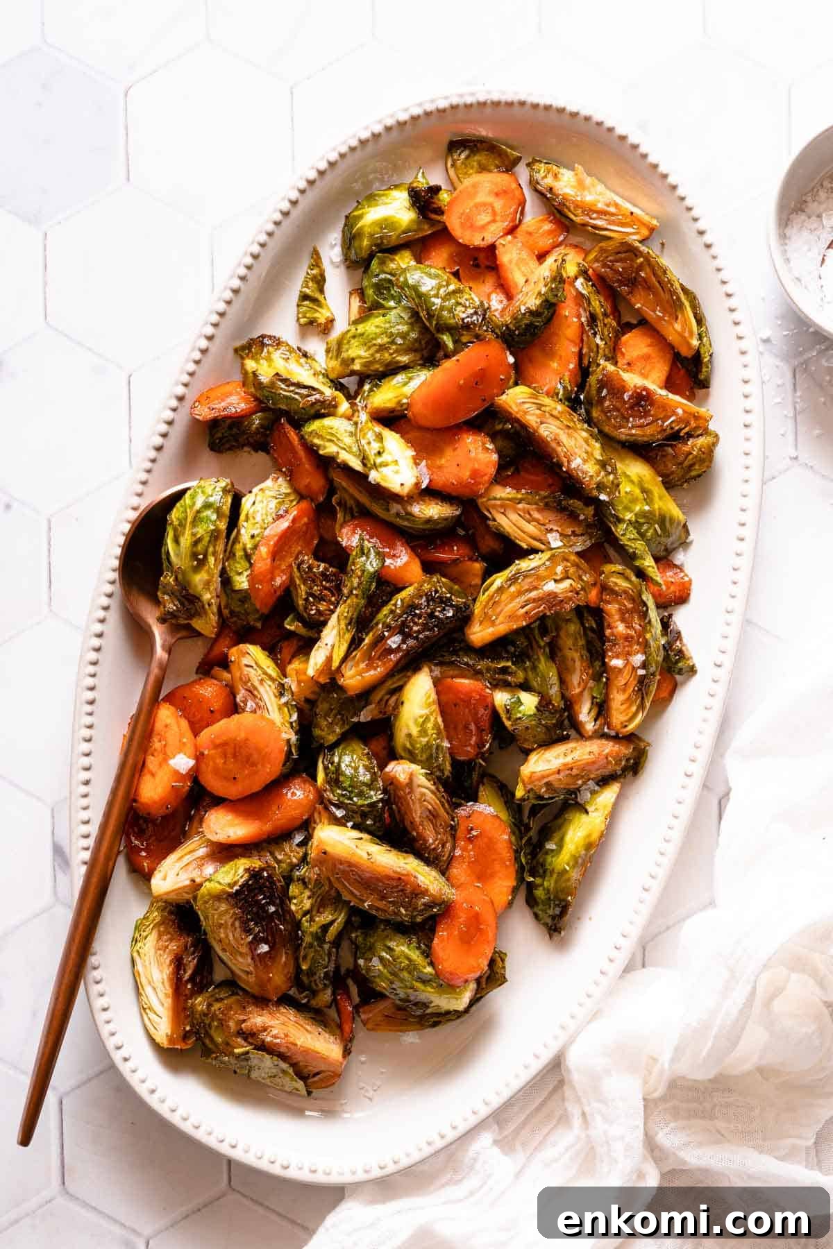 roasted carrots and  brussels sprouts on white platter with spoon on the side