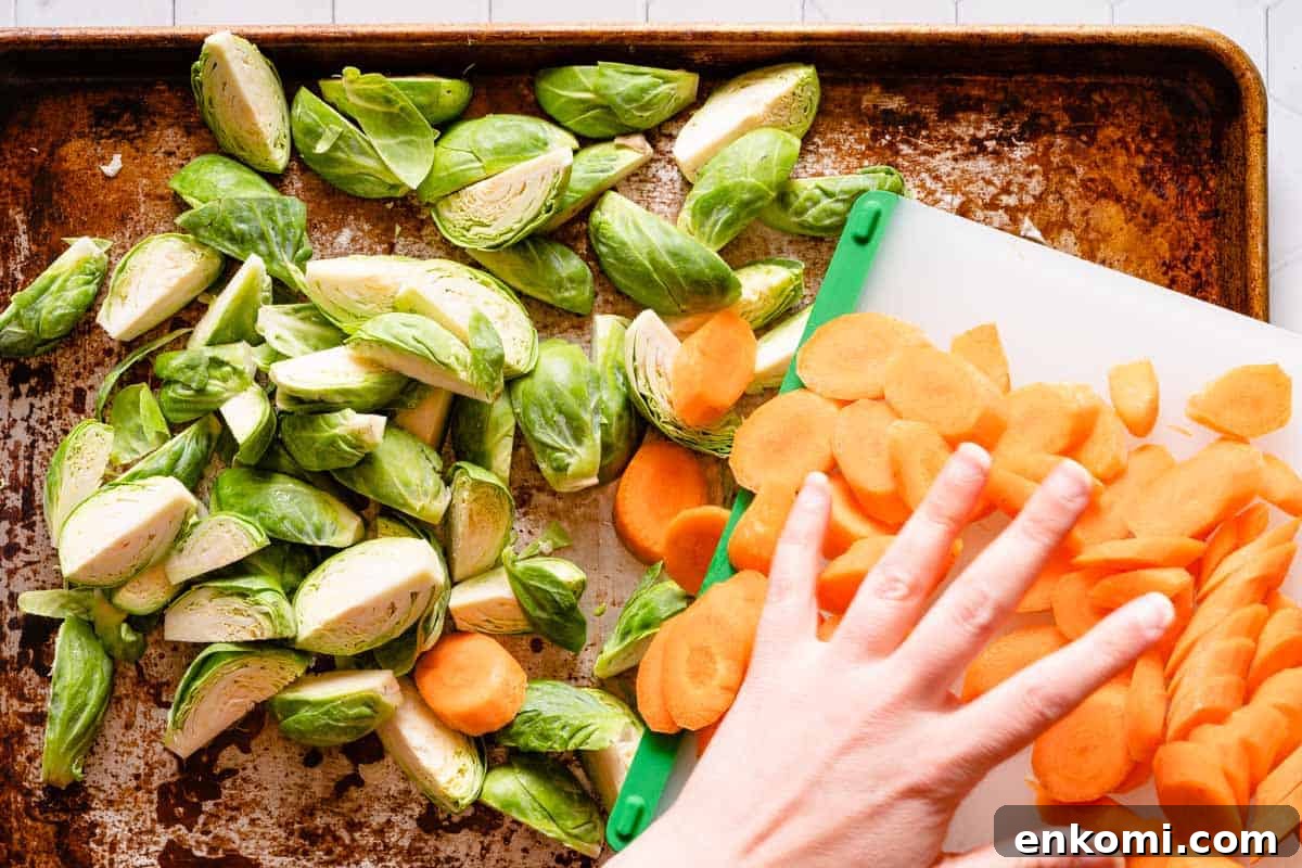 cutting board with sliced carrots being slid onto baking pan filled with quartered brussels sprouts